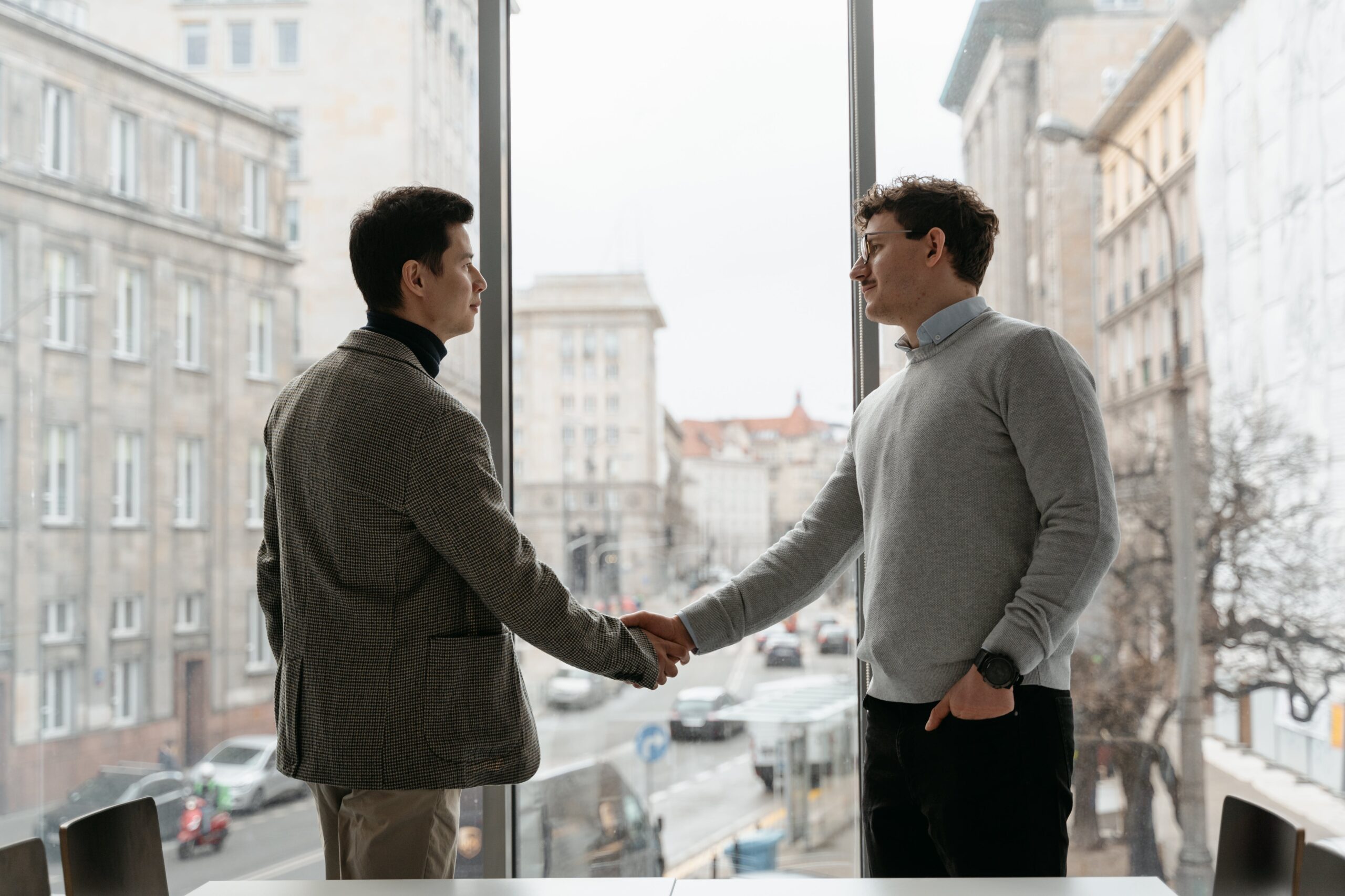 business deal men shaking hands in front of window